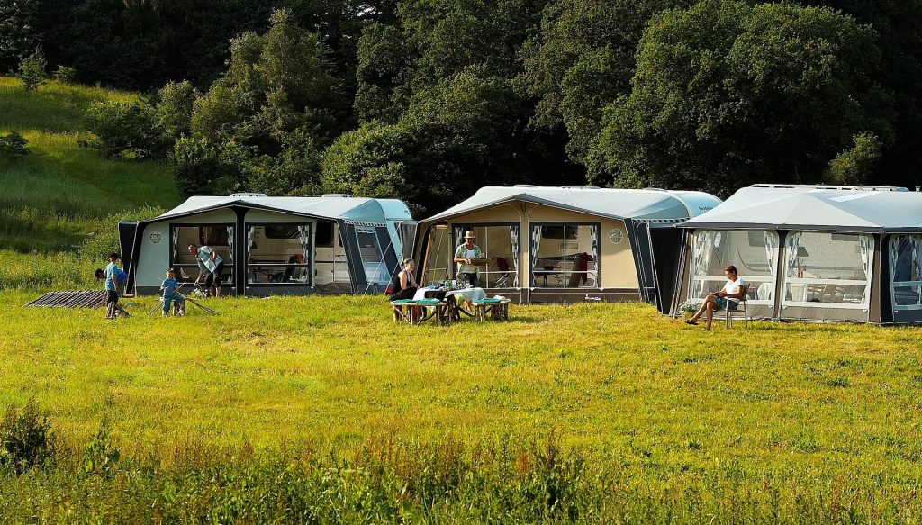 Camping scene met verschillende kampeeroptie's: tent, caravan en camper in een groene natuur omgeving